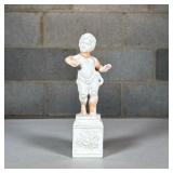Porcelain Putti Figure | Designed as a putti standing on a floral decorated pedestal; no apparent ma