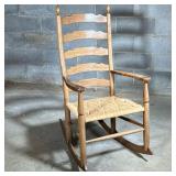 Ladder Back Rocking Chair With Rush Seat | A large rocking chair with a light colored wood frame hav