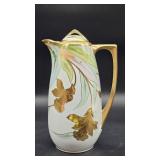 A hand-painted porcelain pitcher signed “Yann” with gilded handle and stylized lily decoration in pa