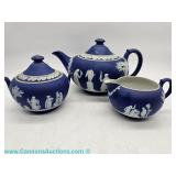 A small, dark blue Wedgwood Jasperware three-piece tea set, consisting of a teapot, creamer, and sug