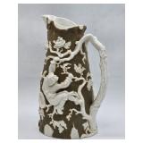 A tall ceramic pitcher molded in a tree trunk form with applied relief of a man climbing among raise