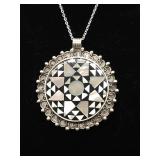 A marked pendant featuring intricate geometric inlay of mother of pearl on a black resin base in a c