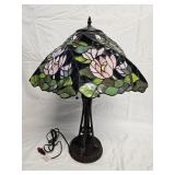Tiffany style stained slag glass table lamp with a floral shade in pink and green tones on a dark gr