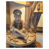 Figural nautical table lamp with sculpted sailor building a model boat at a workbench surrounded by 
