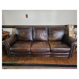 Bassett brown leather three-cushion sofa with rolled arms and nail head trim along the arms and fron