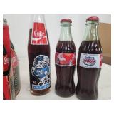 Collection of Vintage Coca-Cola Bottles with Holiday Labels and Wooden Crate