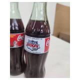 Collection of Vintage Coca-Cola Bottles with Holiday Labels and Wooden Crate
