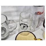 Assorted mugs and glasses including Kimball MN glass mug, Lutsen Glass, Oakley National Bank, Budweiser mugs, and various commemorative mugs