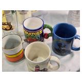 Assorted mugs and glasses including Kimball MN glass mug, Lutsen Glass, Oakley National Bank, Budweiser mugs, and various commemorative mugs