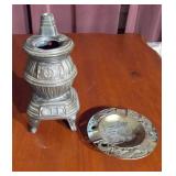 two decorative items: a miniature potbelly stove and a round ashtray.