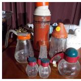The image features a collection of vintage kitchenware, including several glass salt and pepper shakers and a vintage thermos bottle.