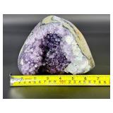 A natural amethyst geode filled with shimmering violet quartz crystals, accented by soft white calcite and encased in its original stone shell.