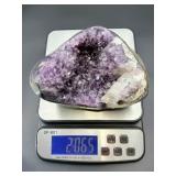 A natural amethyst geode filled with shimmering violet quartz crystals, accented by soft white calcite and encased in its original stone shell.