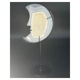 A luminous Botswana Agate druzy carved into a moon shape, showcasing delicate bands of soft gray, caramel, and cream. The sparkling druzy surface catches the light, in a custom metal stand.