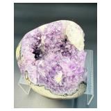 A natural amethyst geode filled with shimmering violet quartz crystals, accented by soft white calcite and encased in its original stone shell.