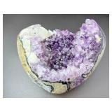 A natural amethyst geode filled with shimmering violet quartz crystals, accented by soft white calcite and encased in its original stone shell.