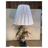 This Lot is a 1970s Hollywood Regency-style table lamp, featuring a sculpted metal base and a pleated shade