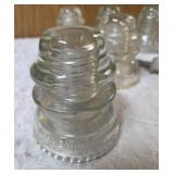 Six vintage clear glass insulators, specifically resembling the Hemingray-45 model based on their shape and color and a pin glass insulator.