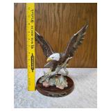 Homco "Majestic Wings" bald10" eagle figurine. It is a porcelain sculpture depicting a bald eagle landing on a rocky mound and is mounted on a dark wooden base with a plaque reading "Majestic Wings". 