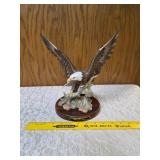 Homco "Majestic Wings" bald10" eagle figurine. It is a porcelain sculpture depicting a bald eagle landing on a rocky mound and is mounted on a dark wooden base with a plaque reading "Majestic Wings". 