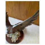 Homco "Majestic Wings" bald10" eagle figurine. It is a porcelain sculpture depicting a bald eagle landing on a rocky mound and is mounted on a dark wooden base with a plaque reading "Majestic Wings". 