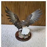 Homco "Majestic Wings" bald10" eagle figurine. It is a porcelain sculpture depicting a bald eagle landing on a rocky mound and is mounted on a dark wooden base with a plaque reading "Majestic Wings". 