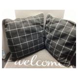 Two Black Throw Pillows and Gray Welcome Mat