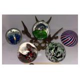 5 ART GLASS PAPERWEIGHTS IN ASSORTED PATTERNS AND COLORS; GREEN PAPERWEIGHT WITH DETACHED BRASS CHERUB STAND