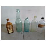 Five old glass bottles, one is broken, two have