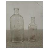 Two old glass medicine bottles, one is marked