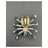 Two tone spider brooch with green rhinestone eyes.