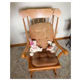 Wood rocking chair with spindle back, shaped arms and brown tufted seat/back cushion. Includes two small plush rabbit figures as shown.