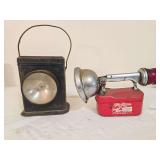 Two vintage electric lanterns including a red Big Beam No. 164 sealed-beam Beacon Lamp and black Big 6 electric lantern with large front reflector and carrying handle. Both show age-related paint and 