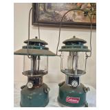 Coleman Models 220J & 228H Lanterns – Marked 12/76 & 12/73. Green double-mantle pressure lanterns with clear globes and wire bail handles, including the wide-ventilator 228H; shows paint wear, oxida