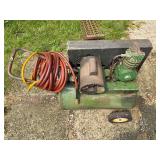Portable wheeled air compressor with horizontal green tank, electric motor, twin-cylinder compressor assembly, pressure gauge and air hose as shown.