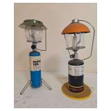 Two portable LP gas lanterns with glass globes, ventilators and carrying handles in differing styles and finishes; shows age-related wear and surface soiling.