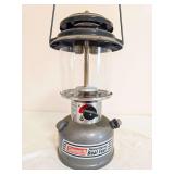 Coleman Model 295-700T Powerhouse Lantern – Marked 2/02. Green painted fount with matching ventilator, clear globe and wire bail handle; shows general age-related use and surface soiling.