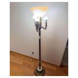 Four-light floor lamp with tall column, decorative metal base, central upward-facing glass torchiere shade and three surrounding light sockets. Shown powered on.