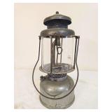 Coleman Air-O-Lantern Model QL pressure lantern with silver-tone fount, dark ventilator, clear Coleman globe and wire bail handle. Shows oxidation and age-related surface wear.