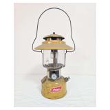Vintage Coleman Model 228H Gold Bond double-mantle lantern with yellow/gold painted fount, matching yellow/gold porcelain ventilator, clear glass globe and wire bail handle. Marked 5/73. Shows paint w