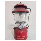 Coleman Model 200A pressure lantern with red fount and red porcelain ventilator, clear globe and wire bail handle; marked 5/67. Shows surface wear, dust and age-related use.