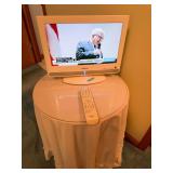 Small Toshiba flat-panel television with Toshiba remote and wood stand as cataloged. Television is shown powered on.