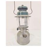 Coleman Model 242A pressure lantern with silver-tone fount, green porcelain ventilator, clear Coleman globe and wire bail handle. Shows age-related surface wear and oxidation.