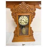 New Haven Clock Co. mantel clock with ornate carved oak case, Roman-numeral dial and decorative lower glass with gold floral and urn design. Includes winding key as shown.