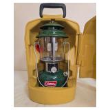 Coleman Model 220J Lantern with Carrying Case. Green double-mantle pressure lantern with clear globe and wire bail handle, housed in a yellow molded Coleman lantern case; shows general age-related use