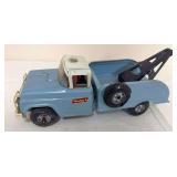 Vintage Buddy L pressed-steel tow truck in light blue and white with rear towing boom and side-mounted spare tire. Shows age-related paint wear and oxidation.