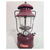 Coleman Model 200A pressure lantern with dark maroon fount, red/maroon porcelain ventilator, clear Coleman globe and wire bail handle; marked 5/62. Shows decal wear, surface wear and age-related use.