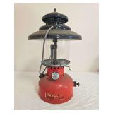Kamplite Model LRL-4 pressure lantern with red fount, black porcelain ventilator, clear globe and wire bail handle. Shows decal wear, paint wear and general age-related use.