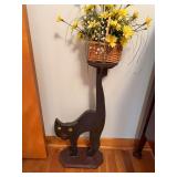 Black cat-form wood plant stand with raised platform and basket of artificial yellow flowers, accompanied by framed prints as cataloged.