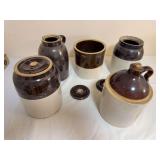 Assortment of brown-and-cream glazed stoneware crocks and jugs with several loose lids as shown. Includes handled and lidded forms with general age-related wear.